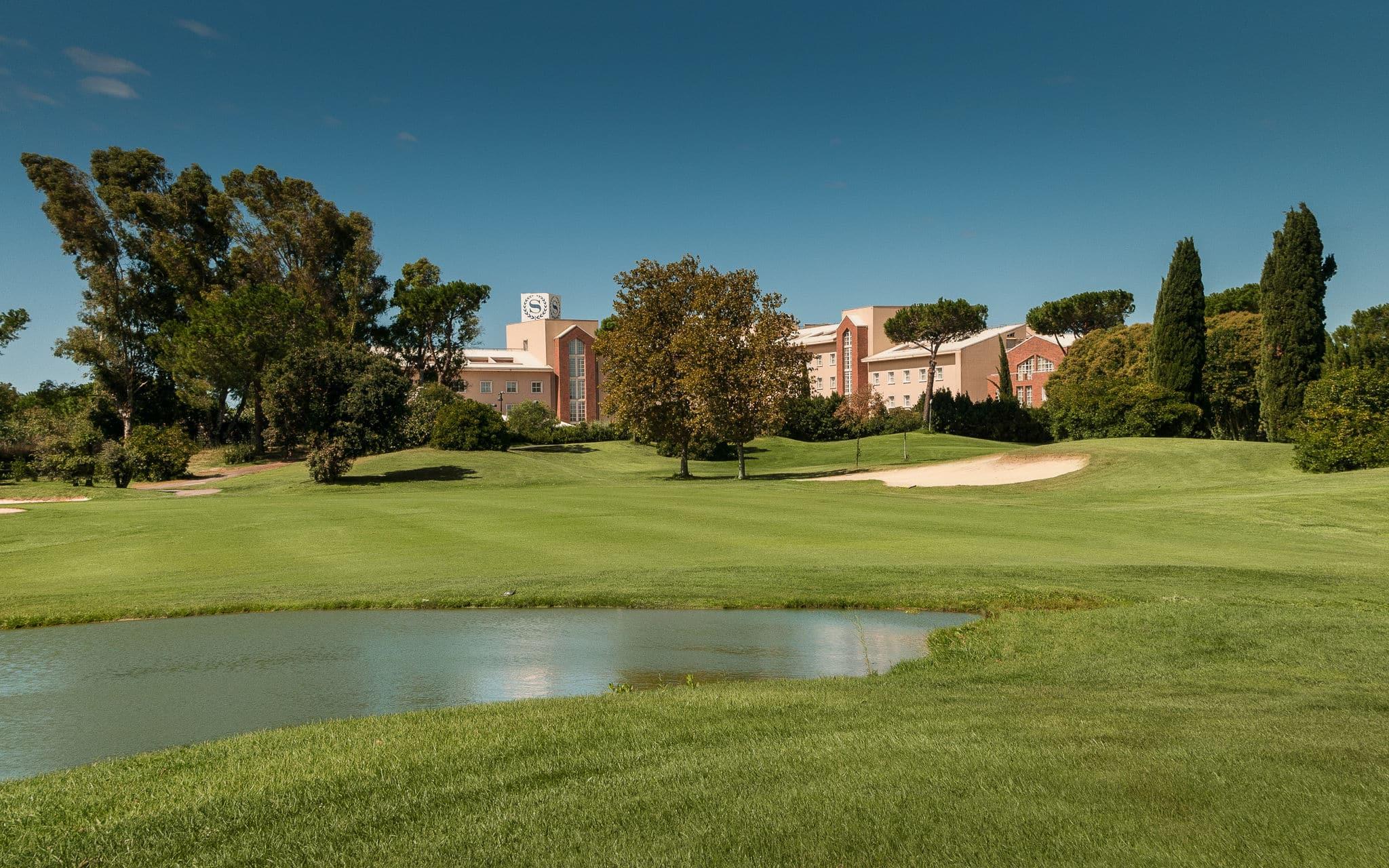A pond and sand traps near the clubhouse on a sunny day.