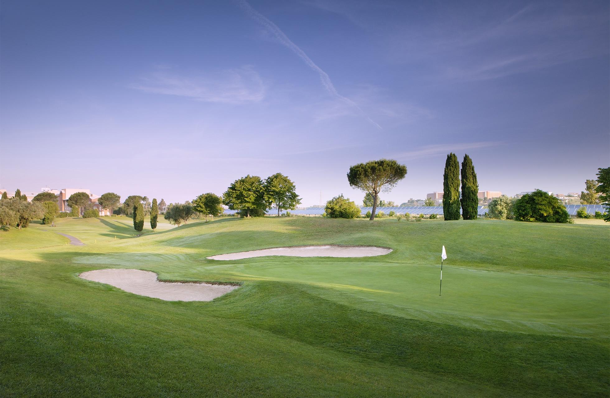 A scenic golf hole with well-maintained bunkers and lush greens under a clear sky.