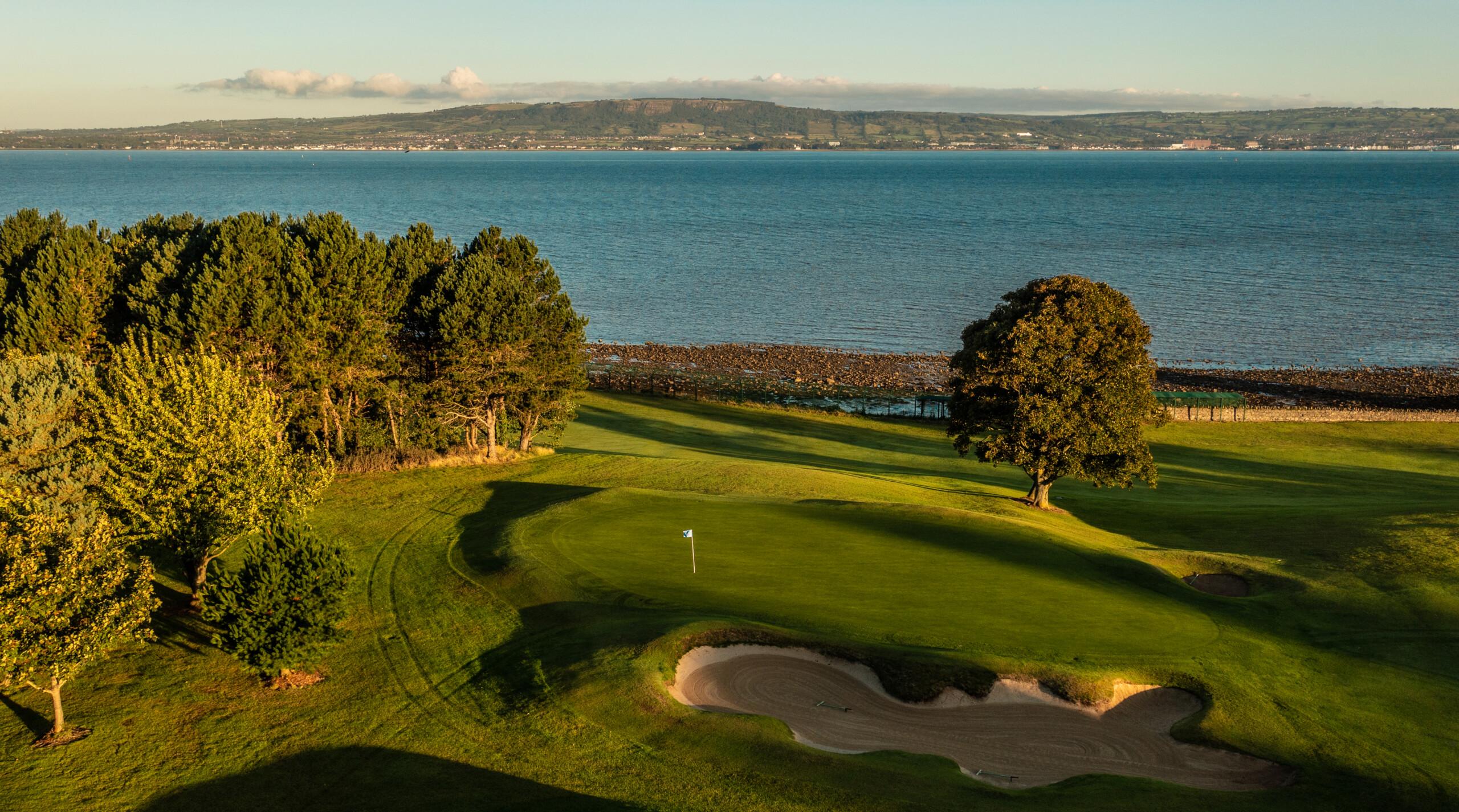 A green nestled near the shoreline with panoramic views across the calm waters of Belfast Lough.