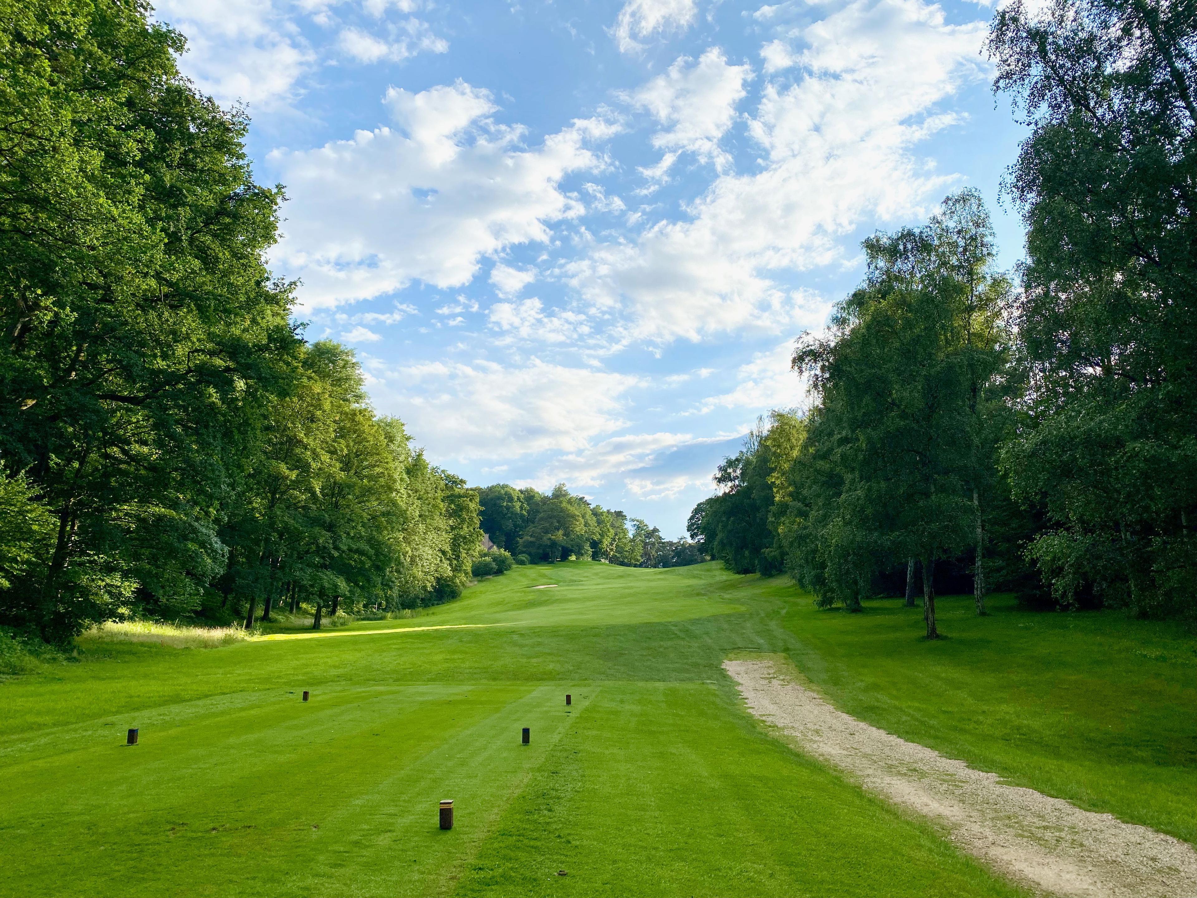 A lush fairway stretches uphill beneath a bright, cloudy sky.