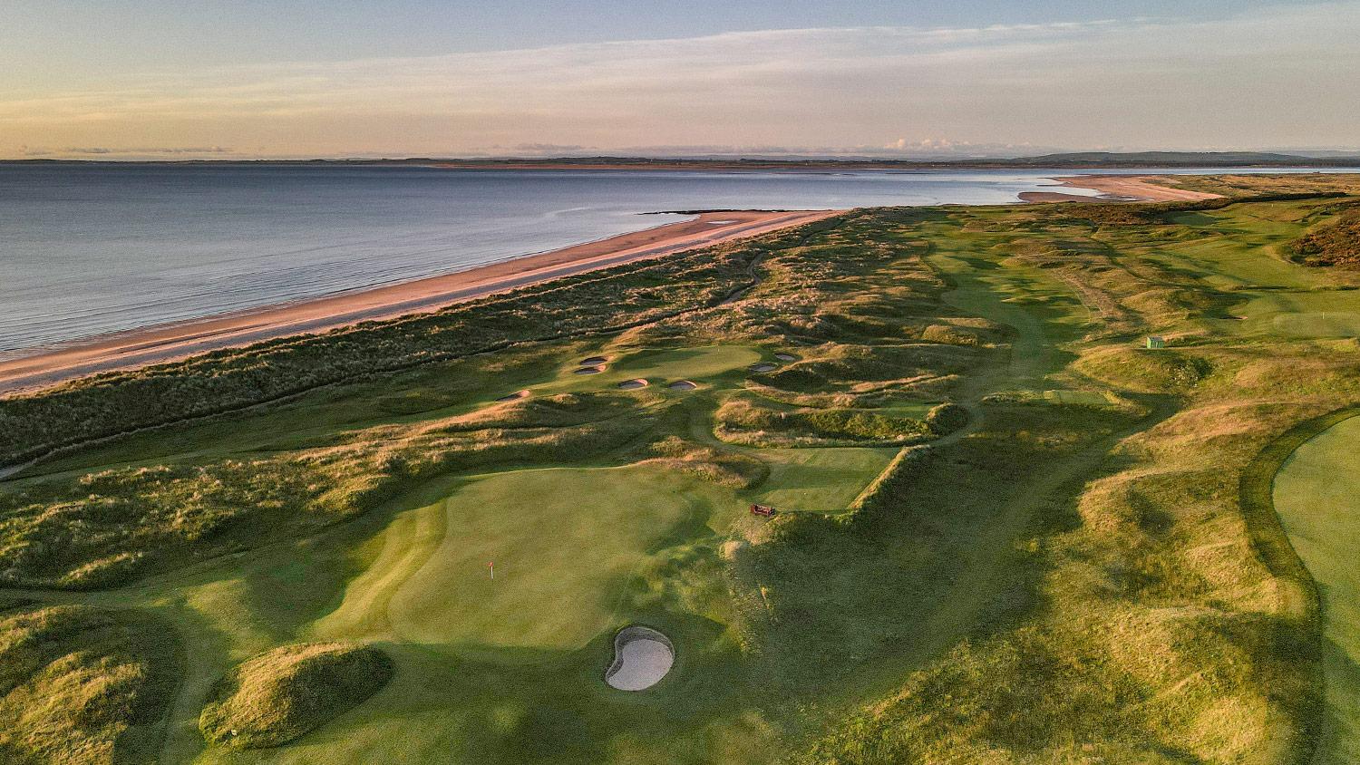 Rolling greens stretch alongside a peaceful beach at sunrise.