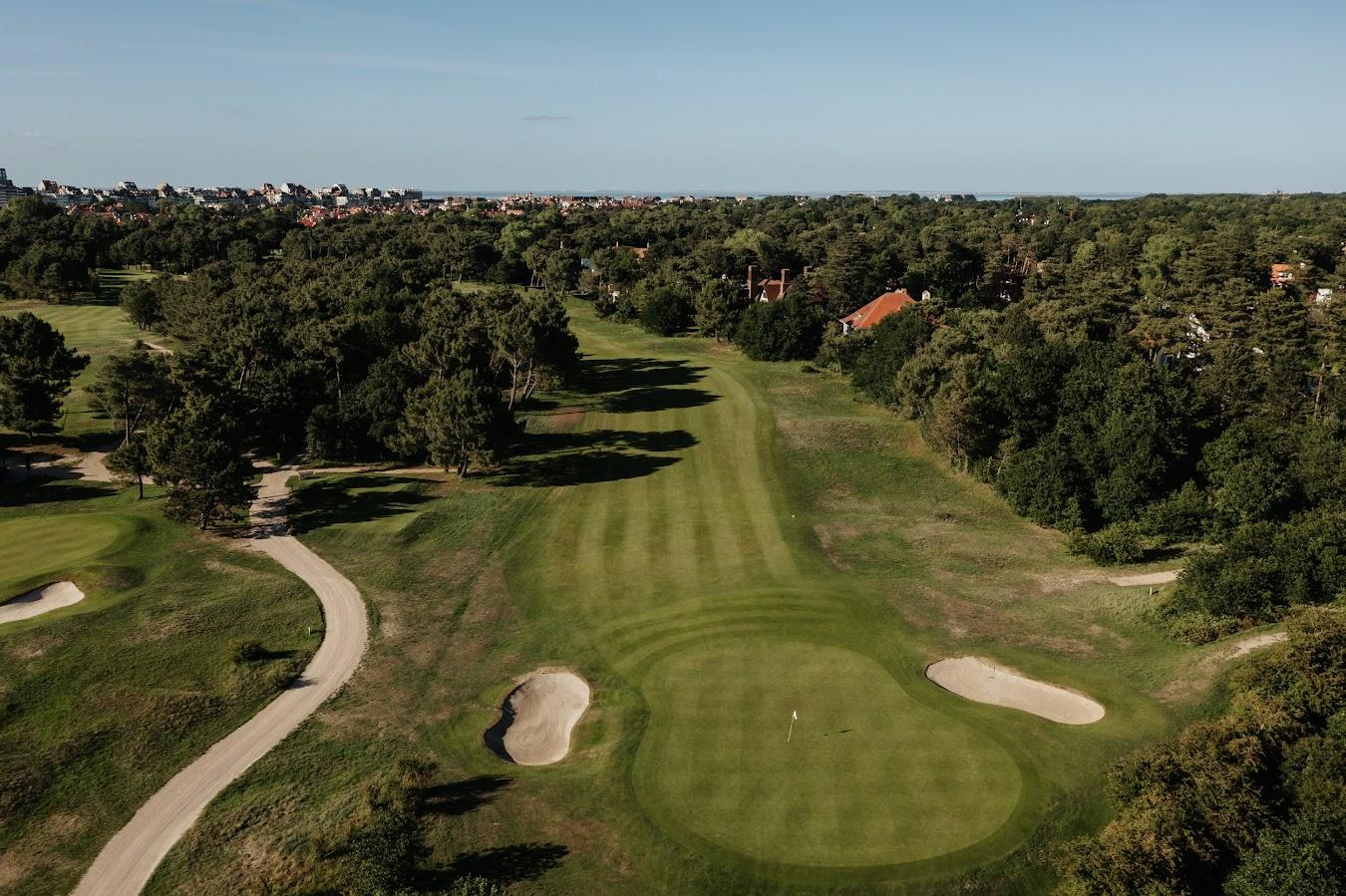 A well maintained fairway leading to a smooth green with forest like trees surrounding
