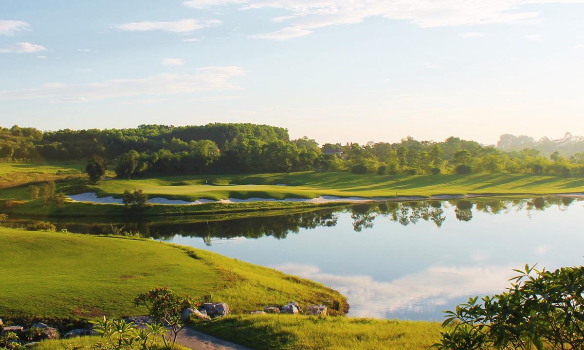 A lathe water hazard reflecting the trees next to a wide fairway nestled with sand bunkers