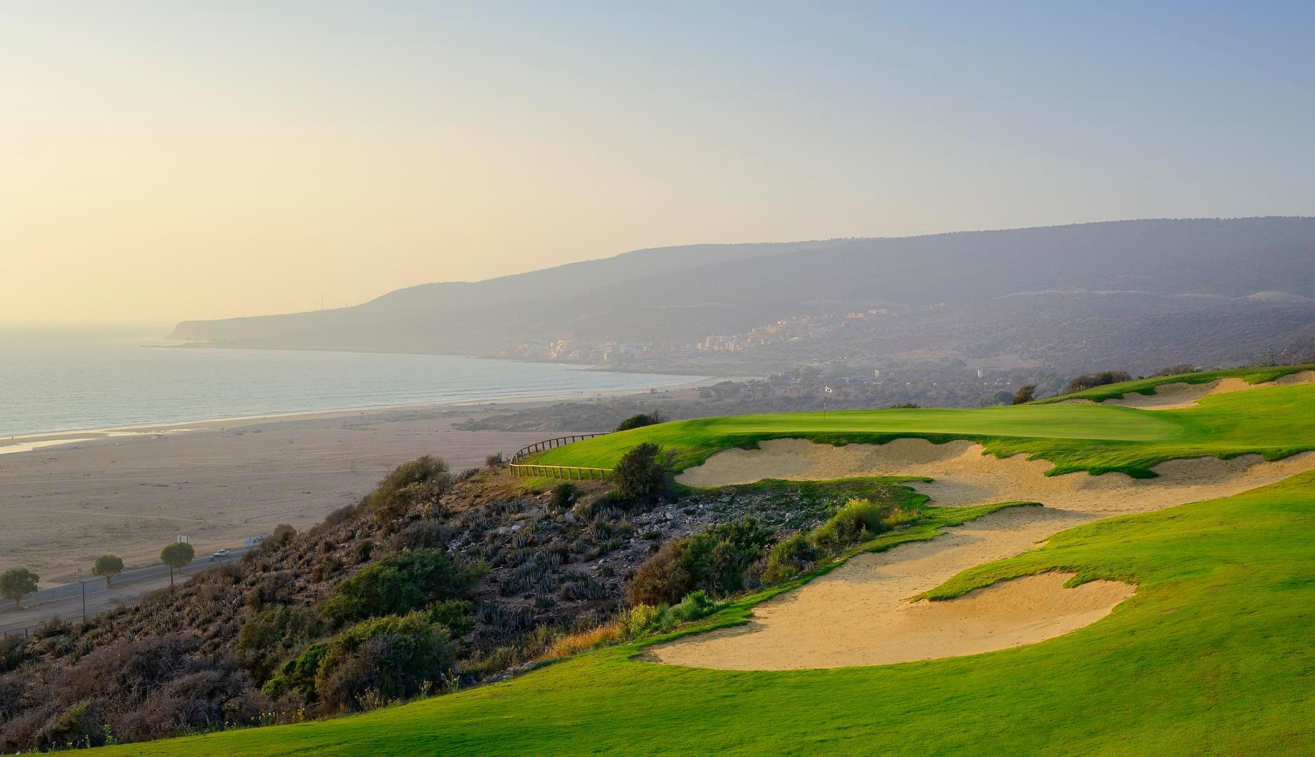 A stunning coastal golf hole surrounded by sand bunkers overlooking the ocean at sunset.