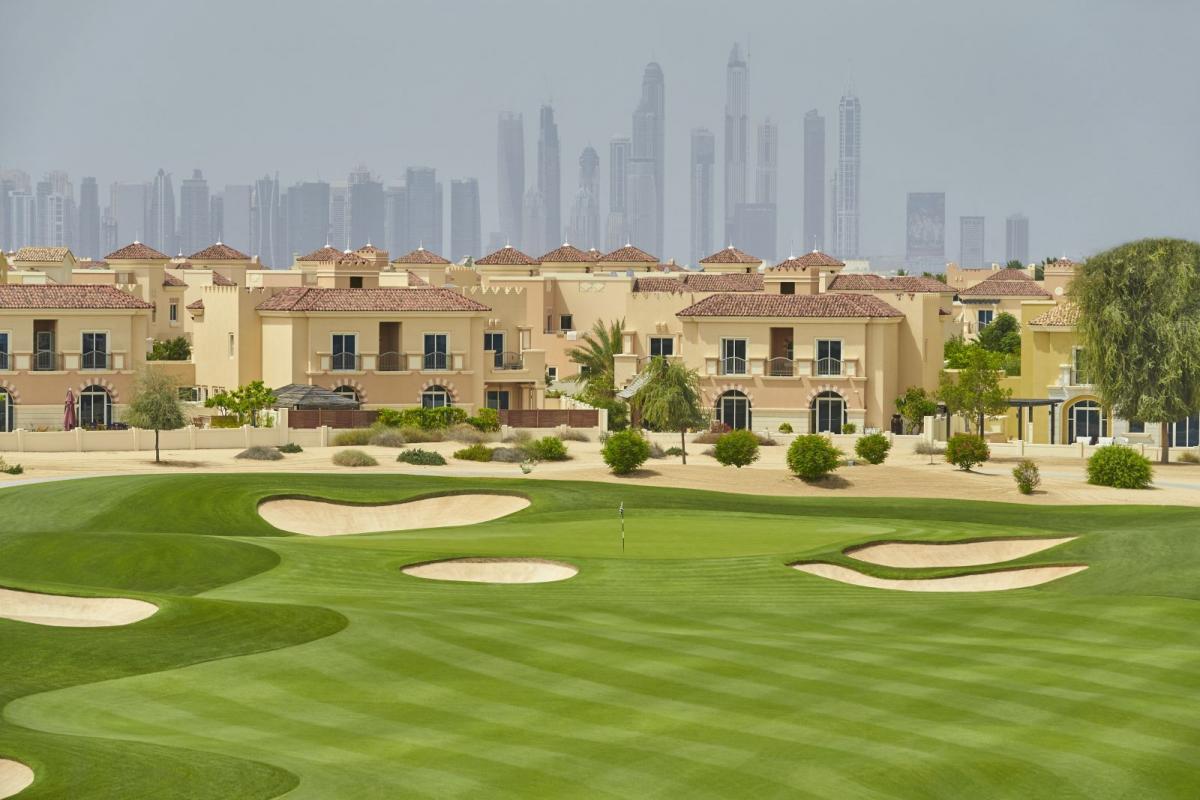 A manicured green surrounded by sand bunkers with houses in the background