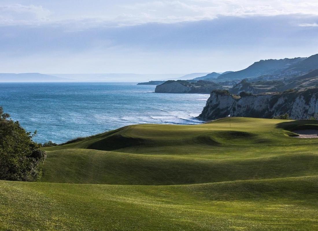 A well kept green surrounded by rolling dunes running along the coast