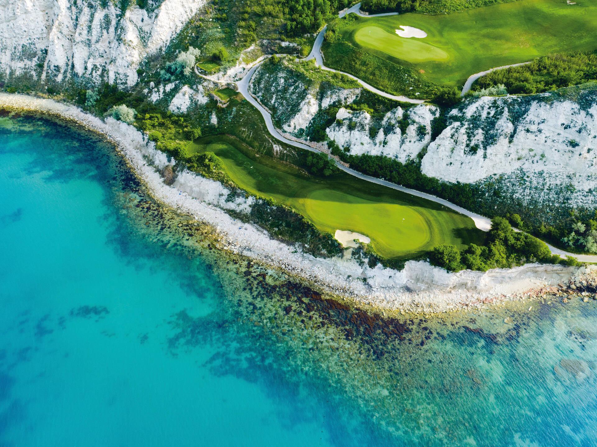 Aerial view of two seaside well-maintained greens on the mountain edge