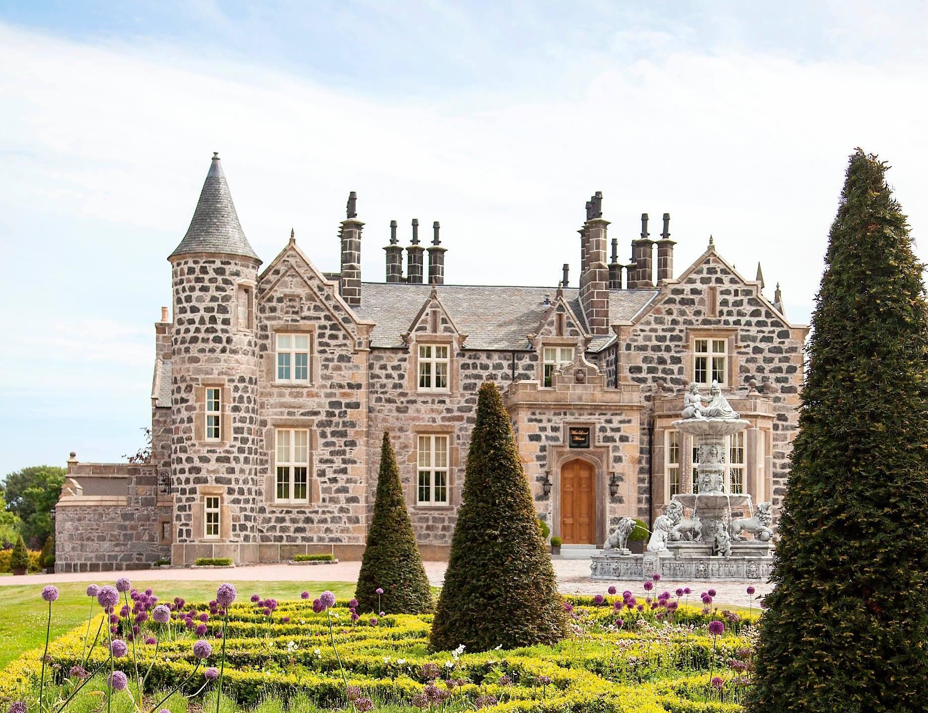 close up view of the castle like building that is the hotel with beautiful garden wand water fountain in the drive