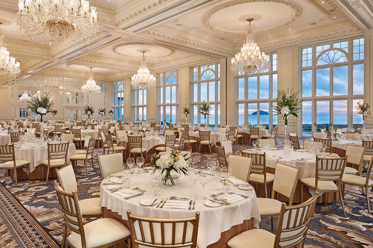 Elegant ballroom set for a grand event with ocean views through large windows.