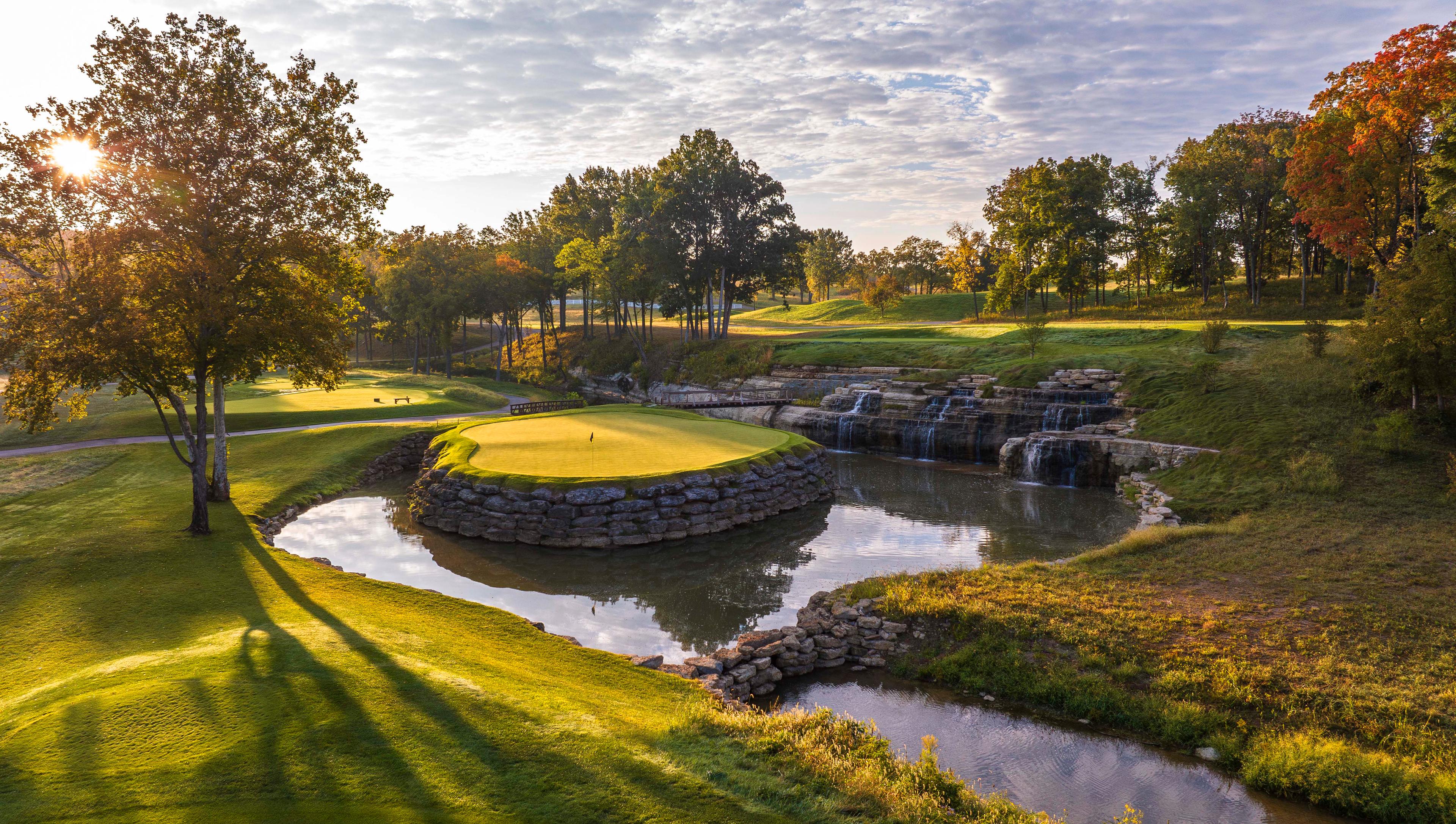 An elevated island green surrounded by water and a rock designed water fall with a bridge to navigate the course under golden sun