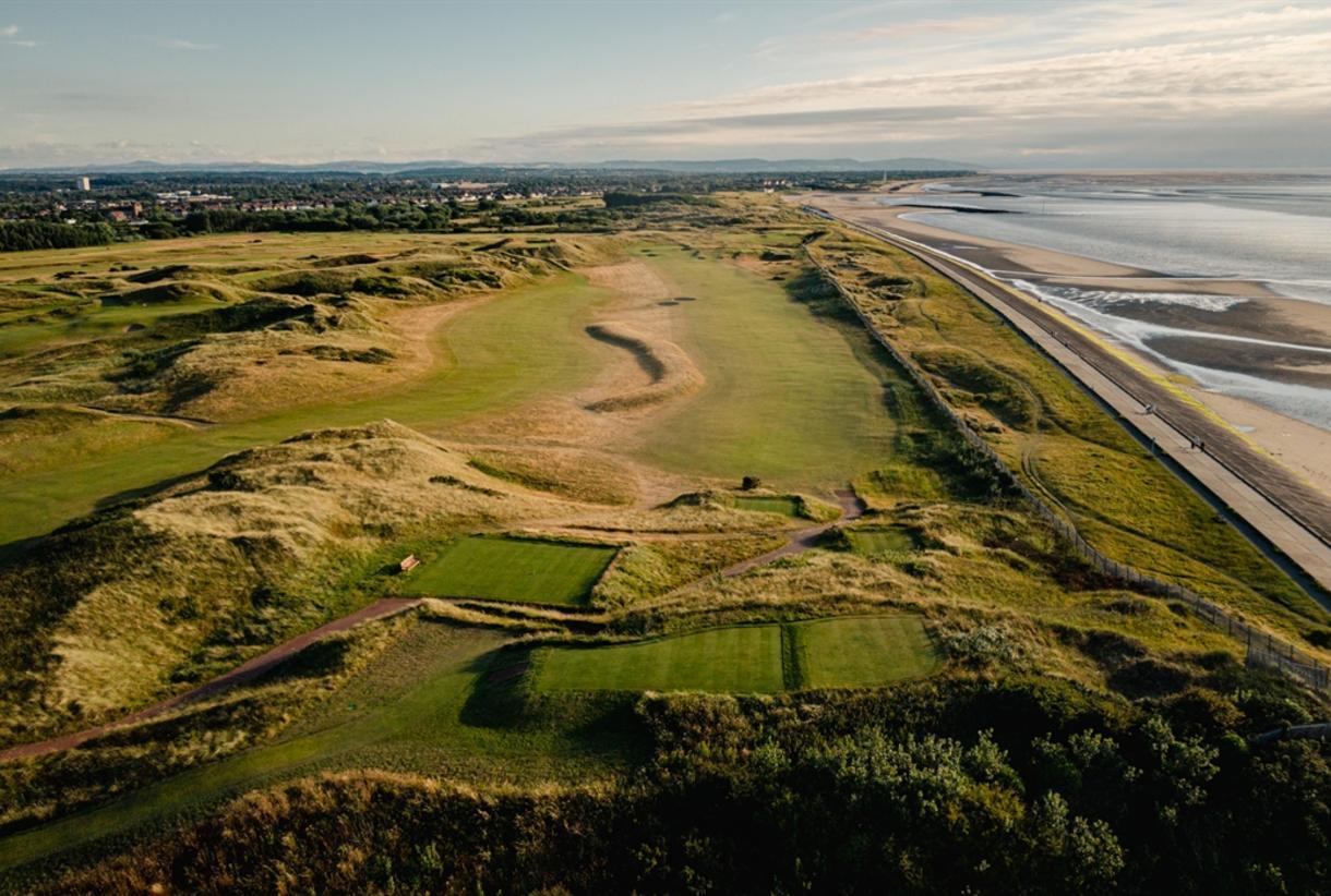 A wide fairway runs parallel to the shoreline, framed by sand dunes and ocean views.
