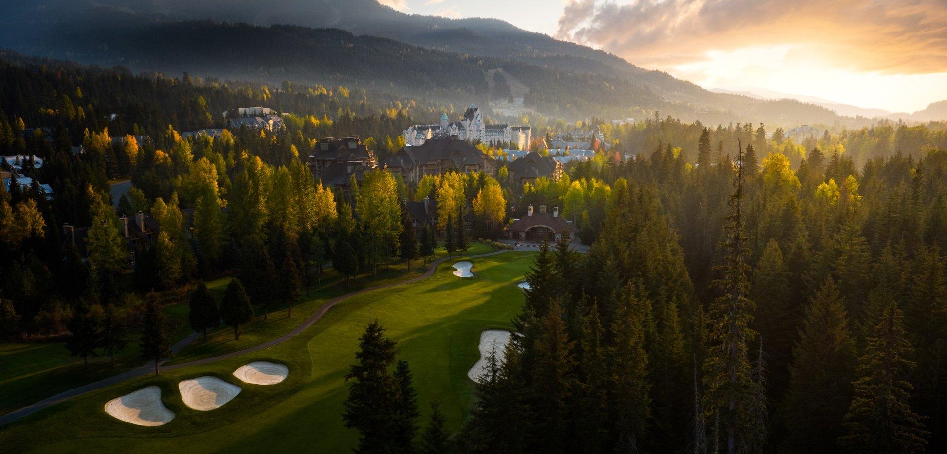 Overhead view of the sun setting over the resort building and course both surrounded by forest trees