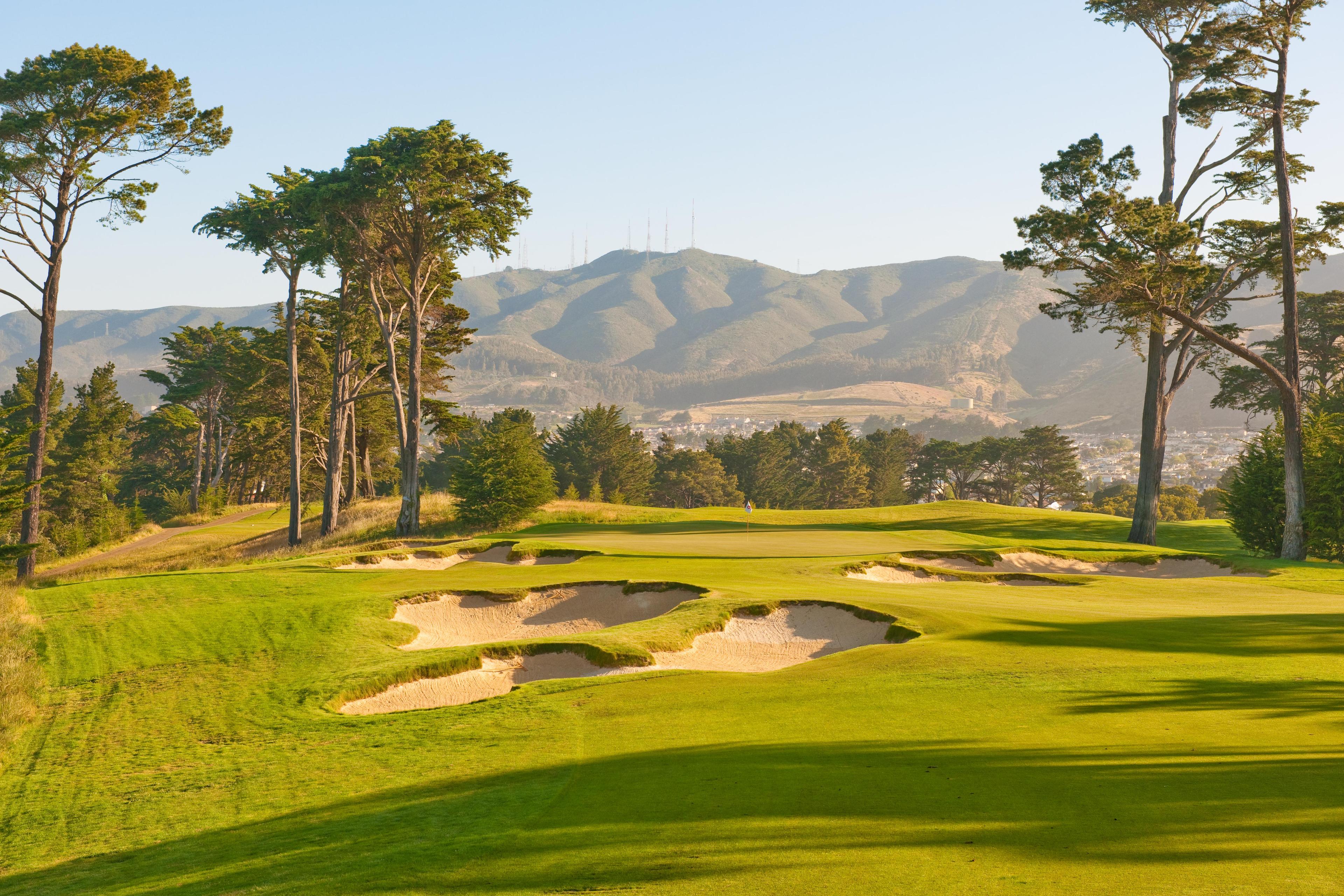 Panoramic view of a manicured fairway littered with sand bunkers surrounded by tall jungle like trees