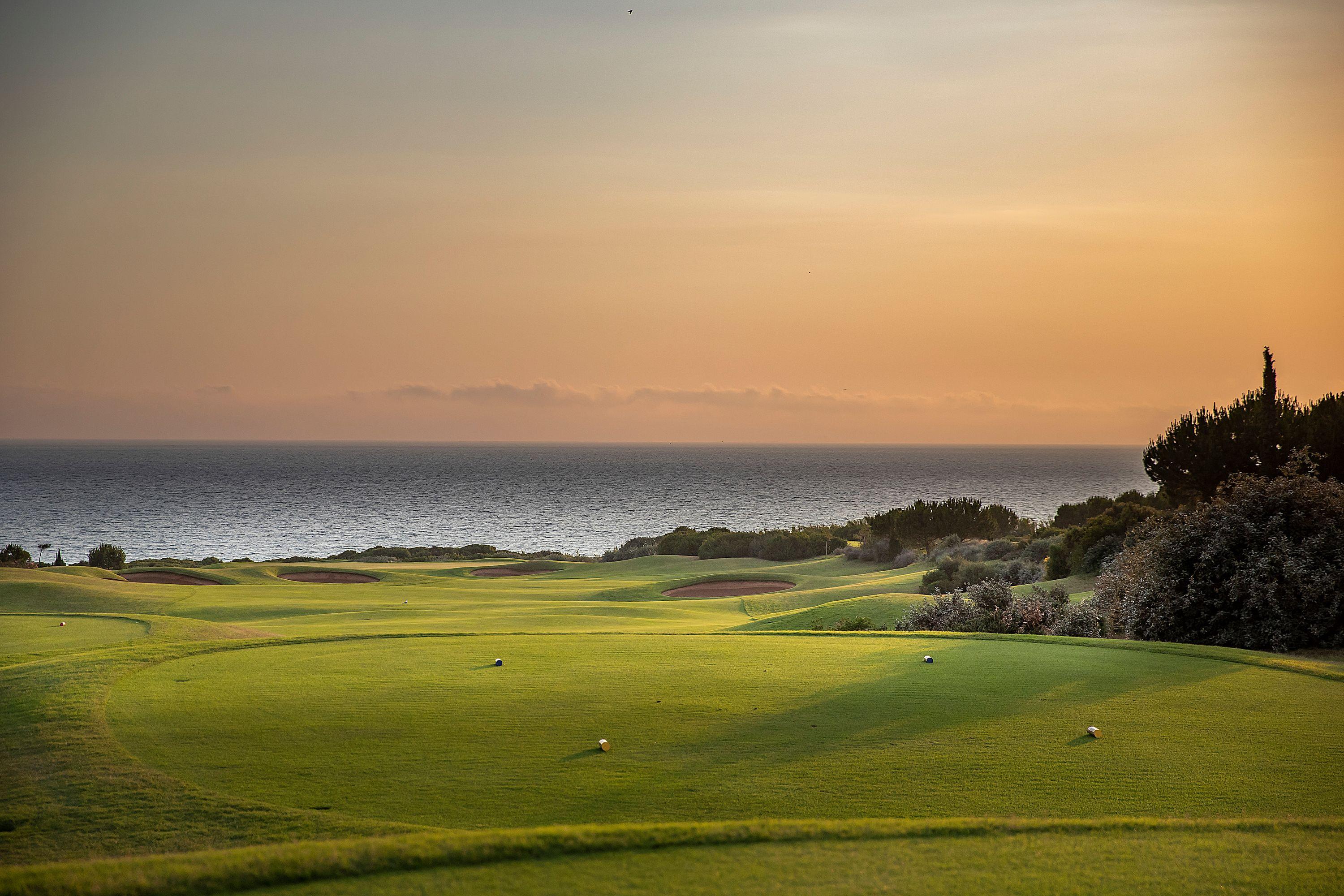 A well maintained fairway leading towards the coast with the sun setting in the distance