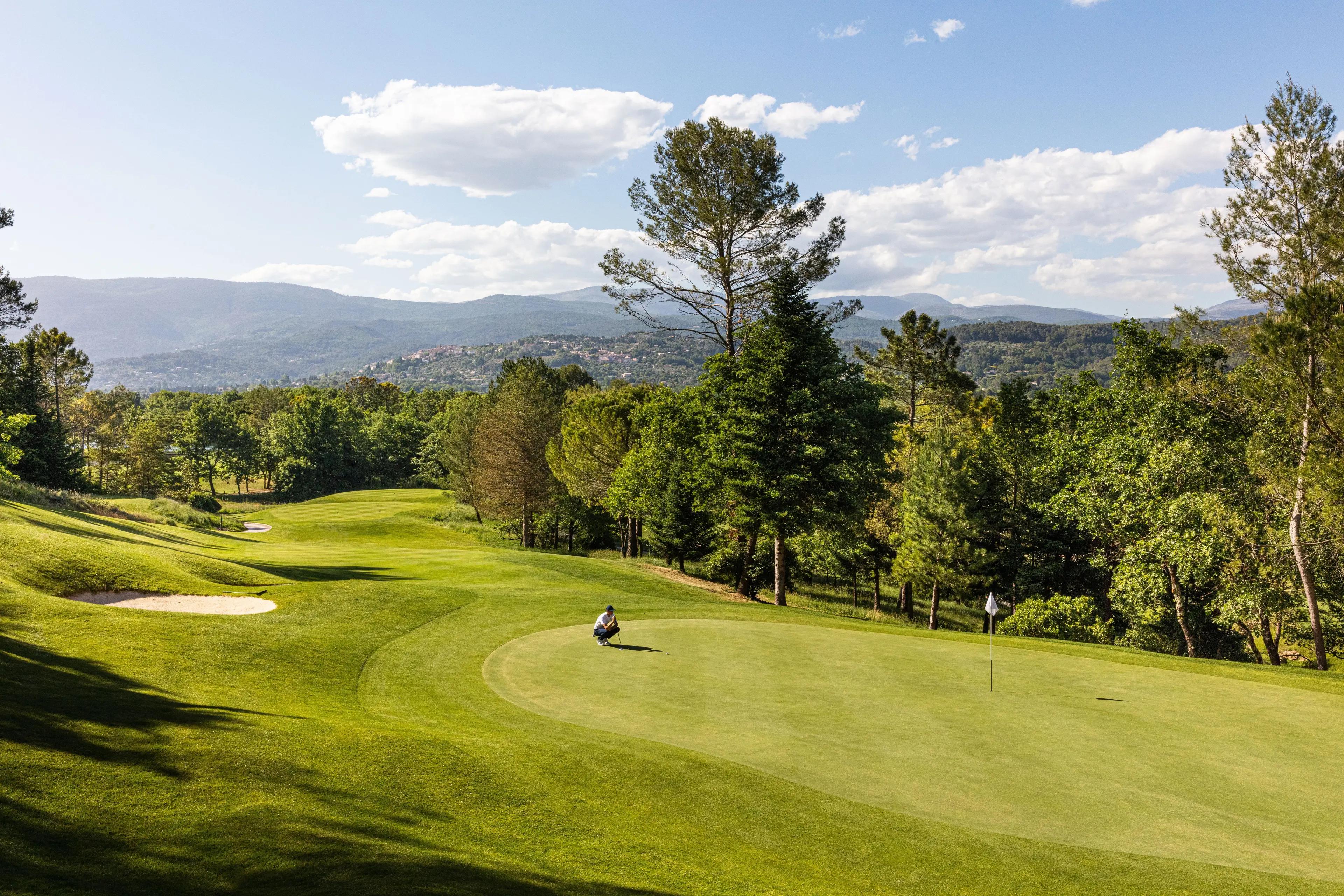 A well maintained fairway leading to a smooth green with a golfer lining up his putt