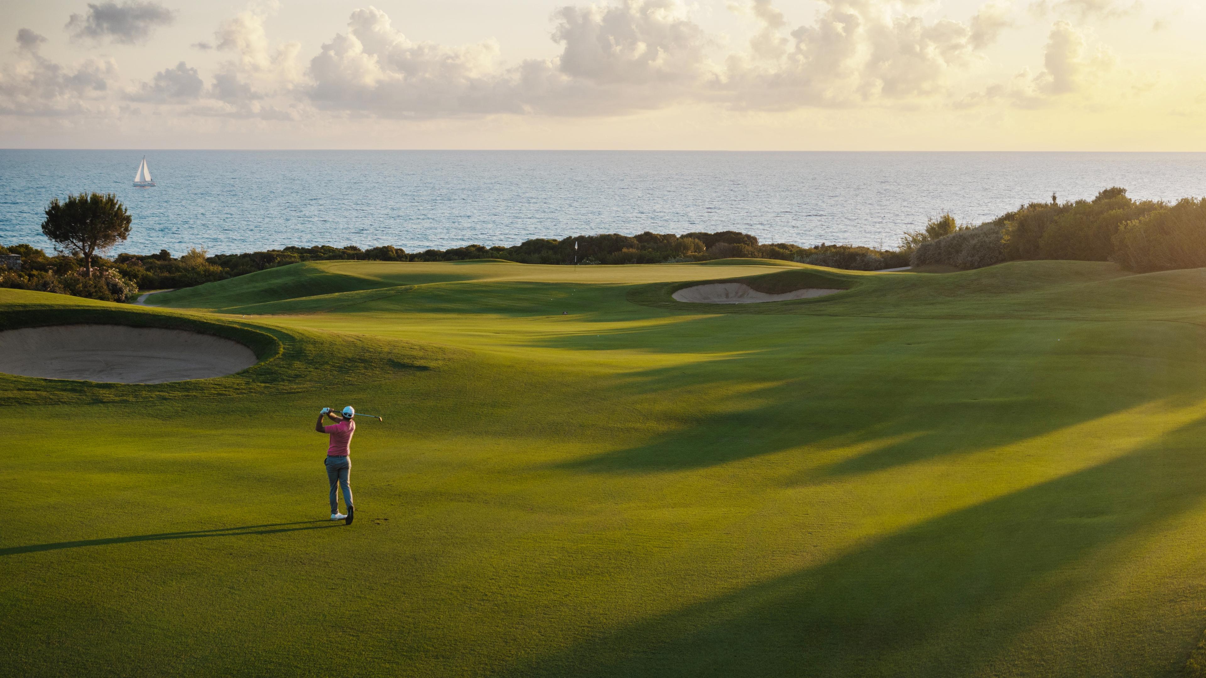 Panoramic view of a well maintained fairway leading towards a smooth green with the sun setting