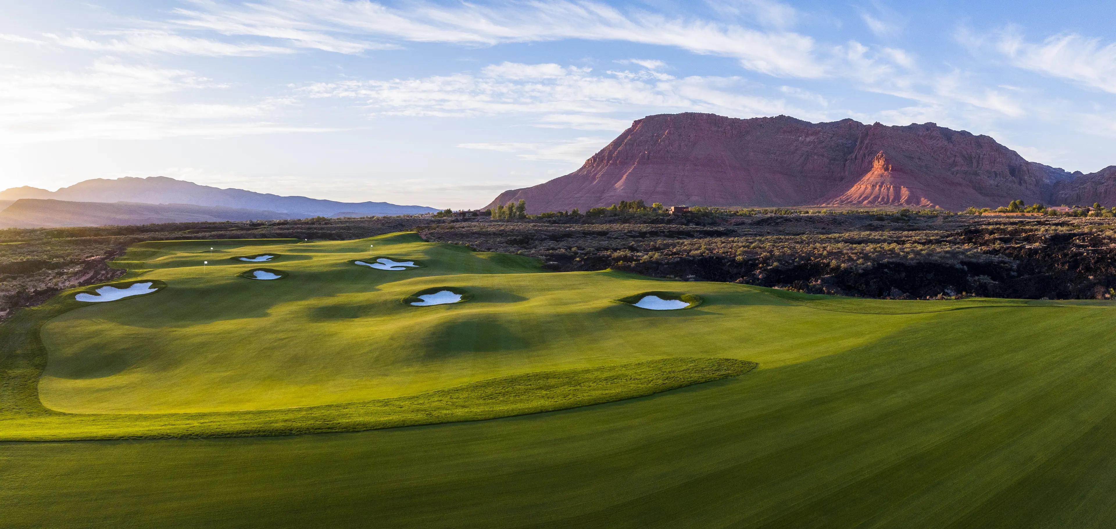 Panoramic view of a well maintained fairway nestled with sand bunkers leading to greens with mountain views in the distaance