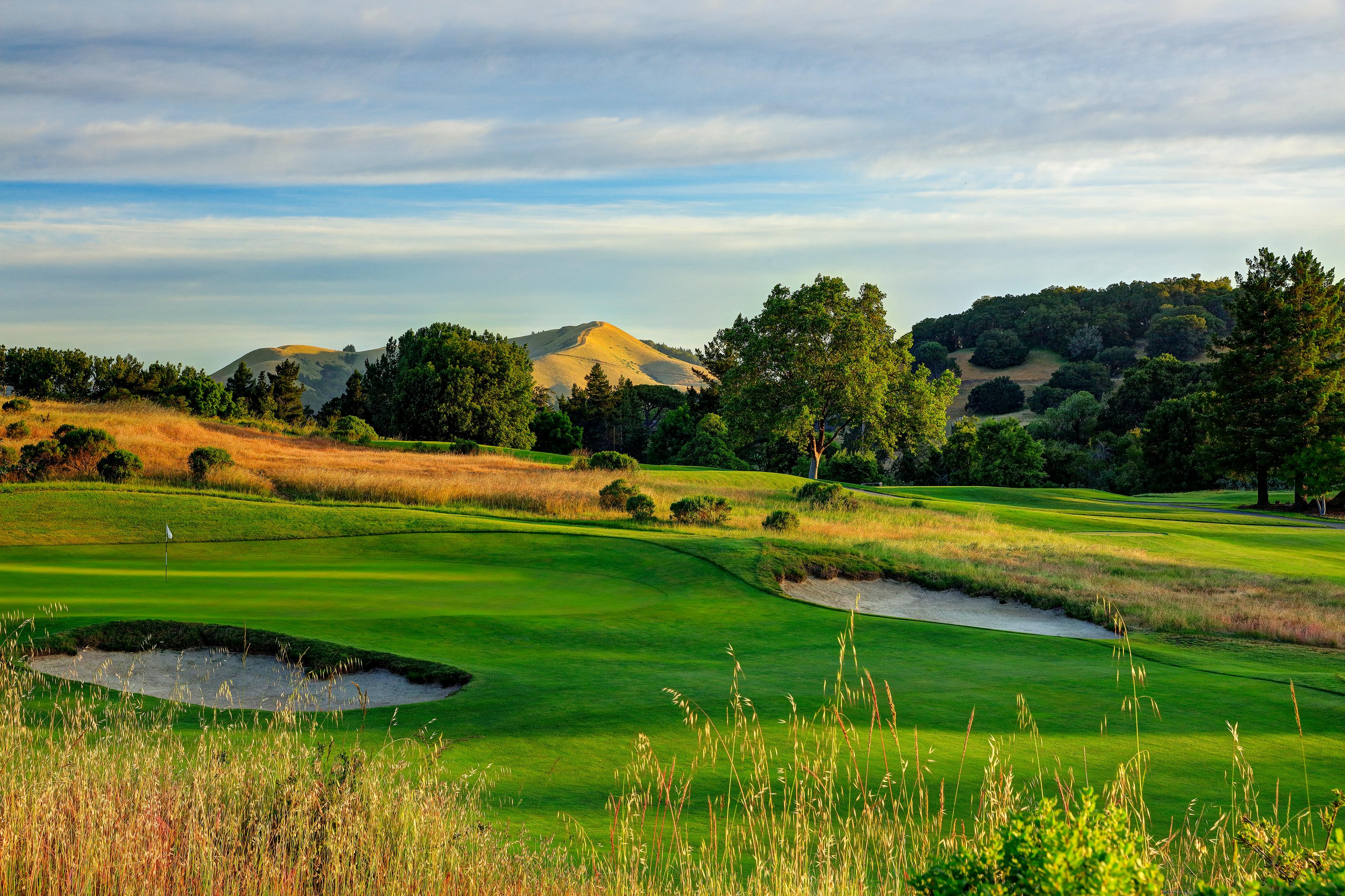 A smooth green surrounded by sand bunkers with distant mountain views