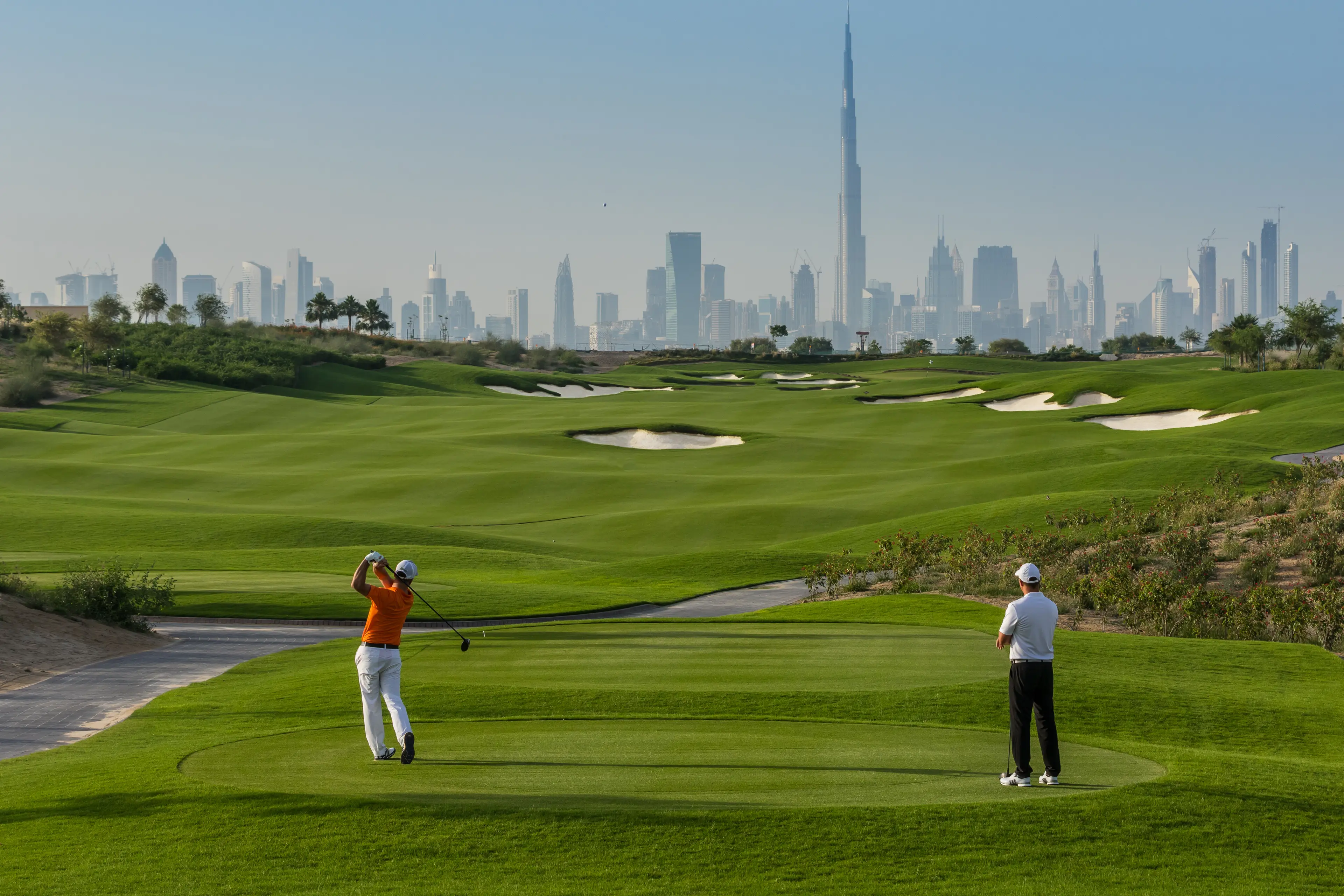 Two golfers on a well maintained fairway nestled with sand bunkers under the Dubai sky line